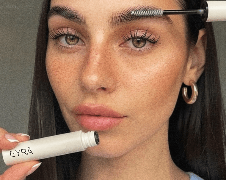 Woman holding EYRĀ lash serum and brow gel